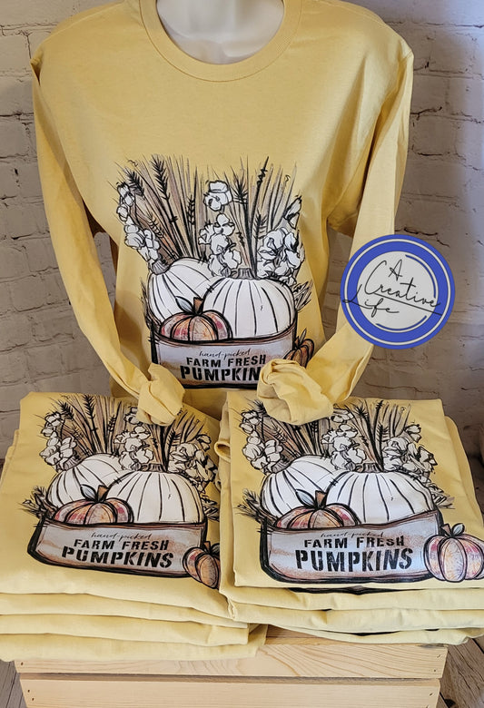 A display of yellow long-sleeve t-shirts with a farm and pumpkin design, stacked on a wooden rack.