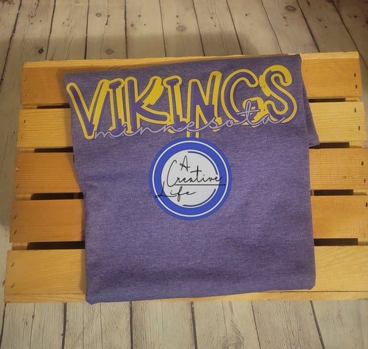 A purple t-shirt with 'Minnesota Vikings' text in a graffiti front, placed on a wooden bench.