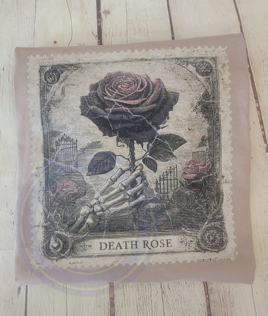 Decorative pillow with skeleton hand holding a rose and 'Death Rose' text on a wooden surface.