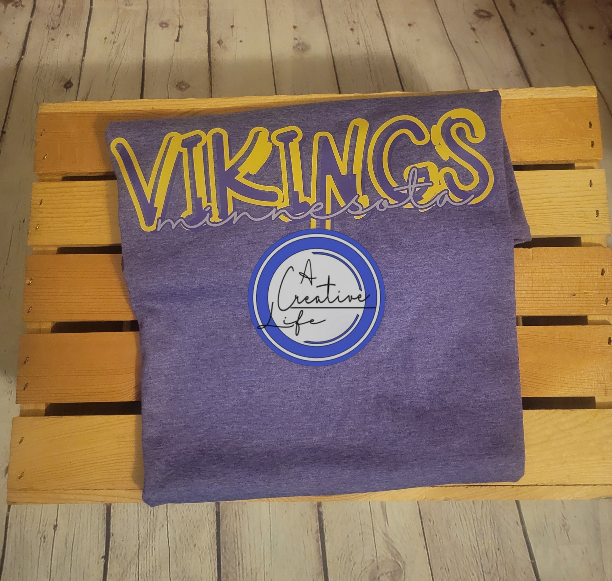 A purple t-shirt with 'Minnesota Vikings' text in a graffiti front, placed on a wooden bench.